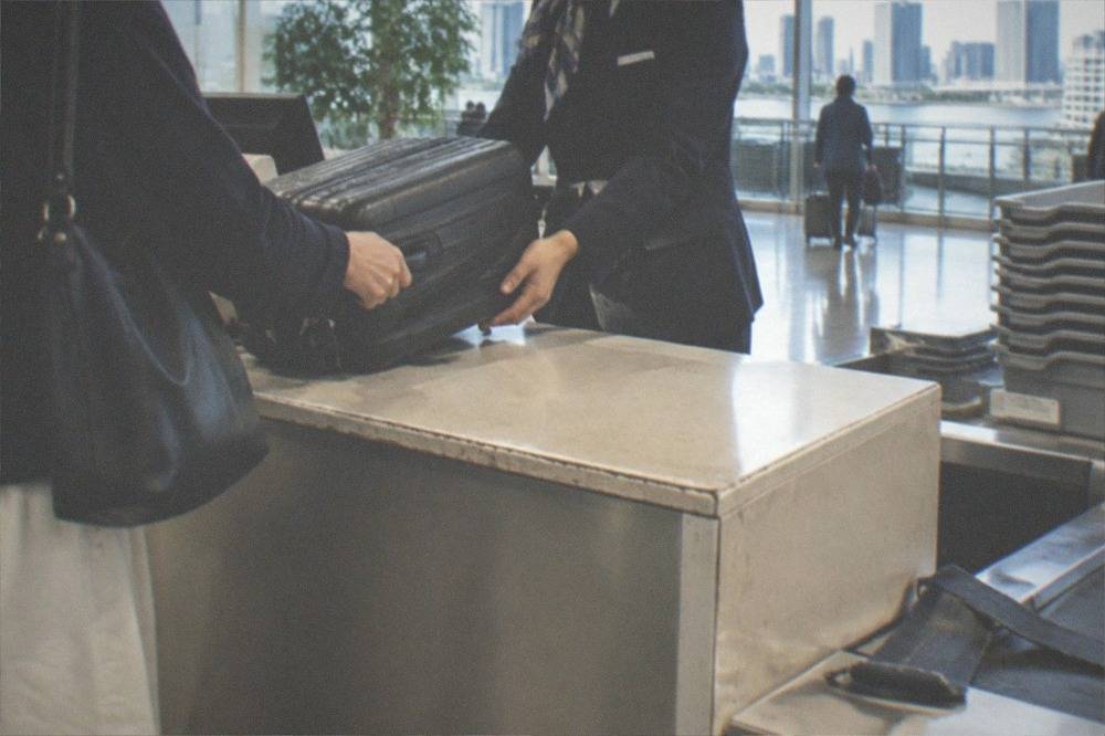 A staffed luggage storage counter with a suitcase being handed over inside an airport terminal