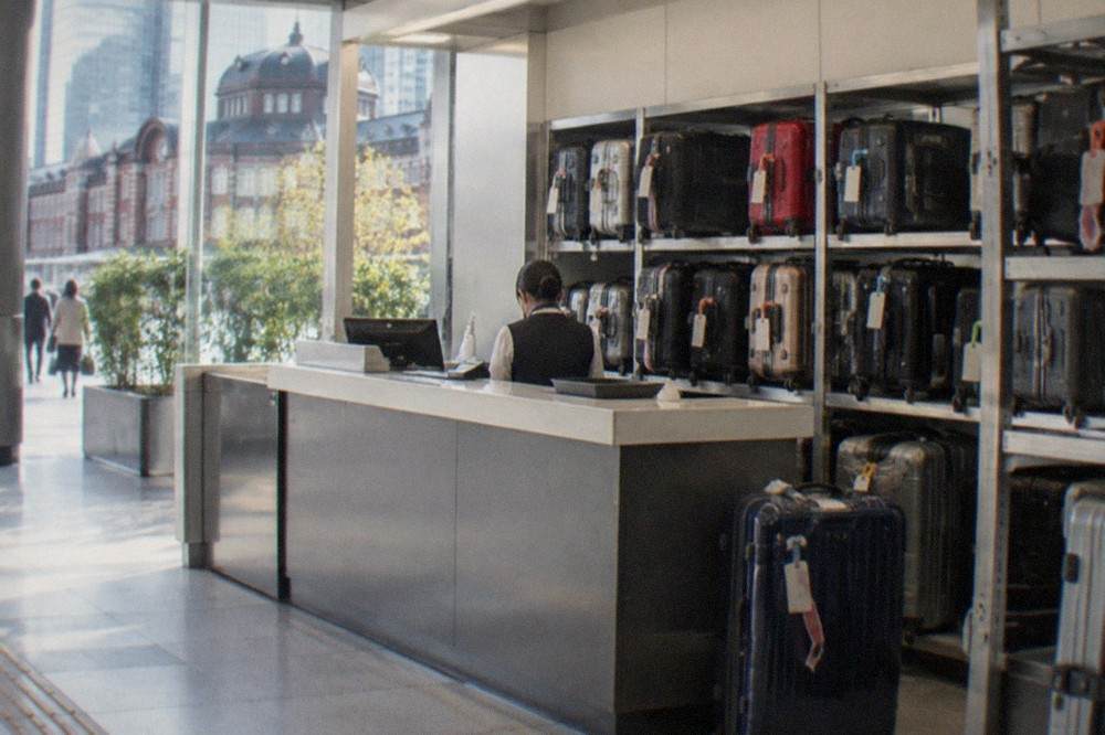 Baggage storage counter in an airport terminal with a staffed desk and stacked suitcases beside it
