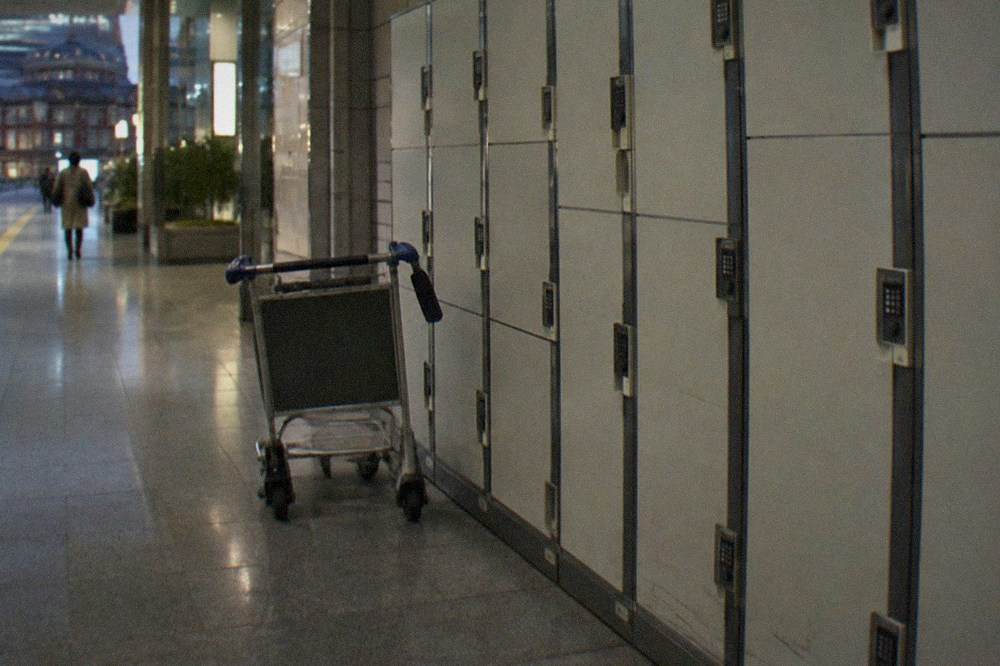 Row of coin lockers along an airport corridor with numeric keypads and a luggage trolley parked nearby