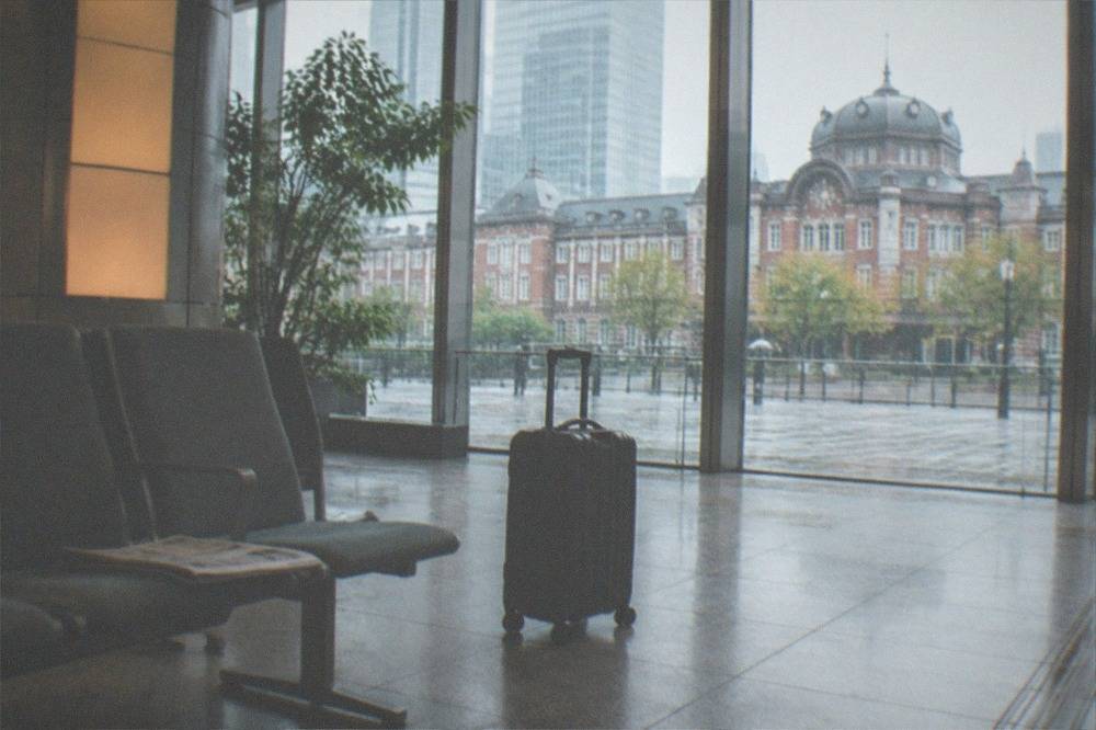 Suitcase standing beside a departure board in a quiet airport lobby with wide windows and empty seating