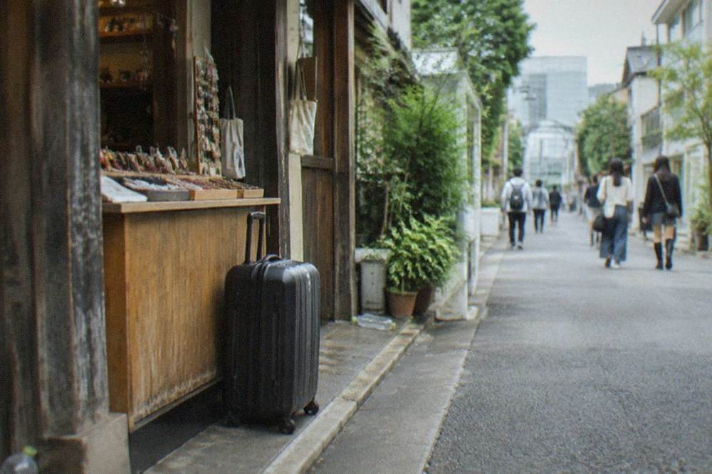 A suitcase parked beside a shop counter in a Tokyo shopping street, ready for a same-day drop-off.