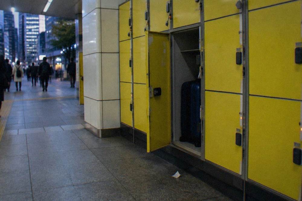 A yellow coin locker bank in a Japanese station with one door open showing a suitcase inside