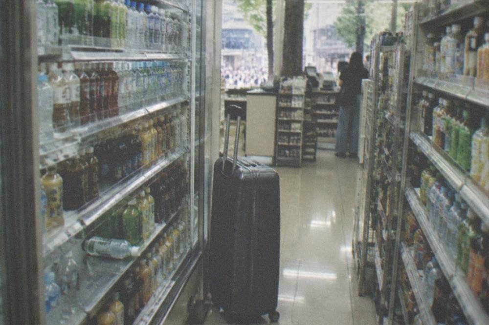 A large suitcase standing in the aisle of a Tokyo convenience store beside shelves of drinks