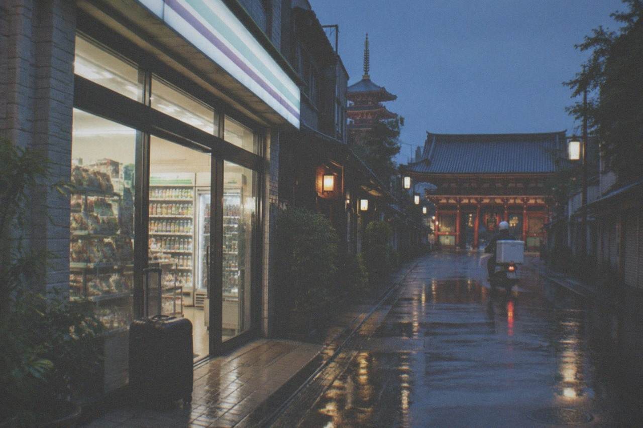 A Seven-Eleven storefront in Tokyo at dusk with a suitcase parked beside the entrance