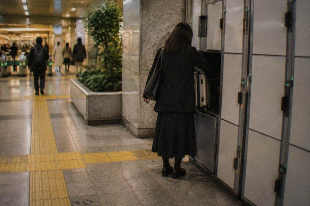 a traveller placing a small suitcase into an open coin locker in a Tokyo subway station