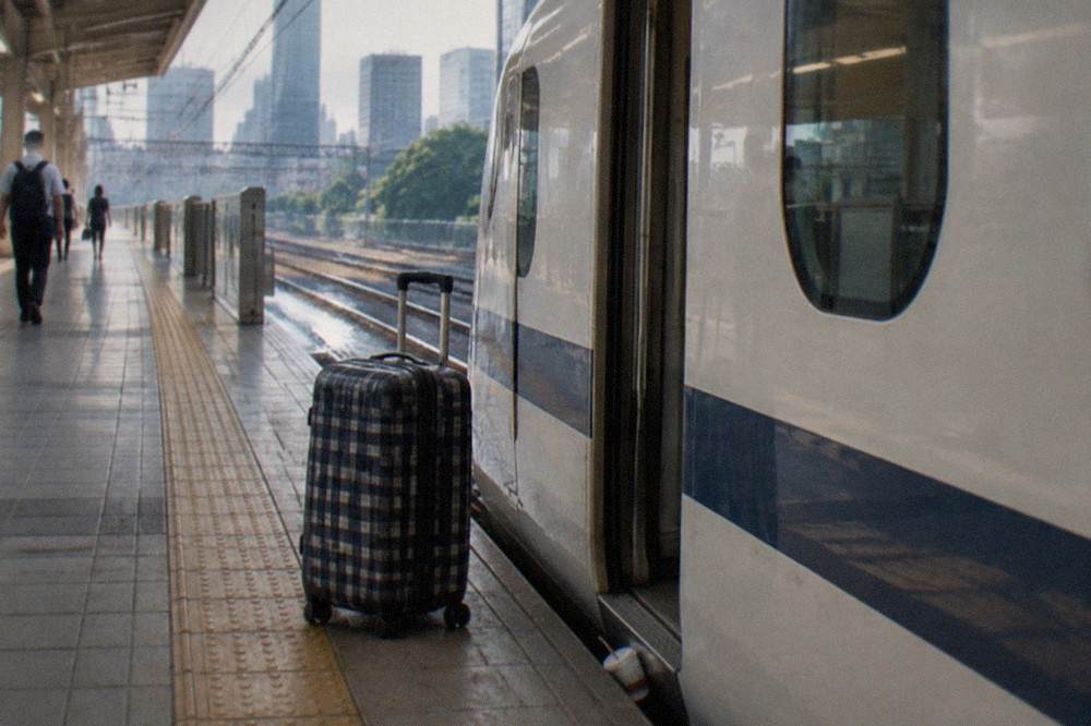 A large checked suitcase standing beside a train door on a Japanese high-speed rail platform