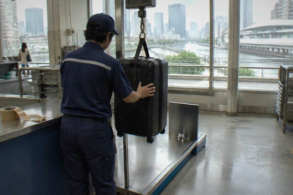 An airport luggage delivery counter sign with a courier weighing a suitcase