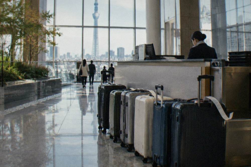 Suitcases parked in a row beside a staffed bag drop counter in a Tokyo shopping complex