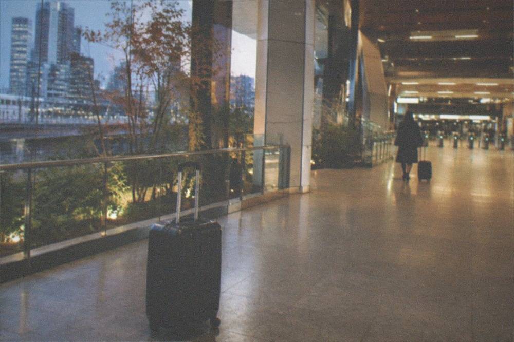 A lone suitcase standing on an airport terminal concourse beside departure signage in the evening