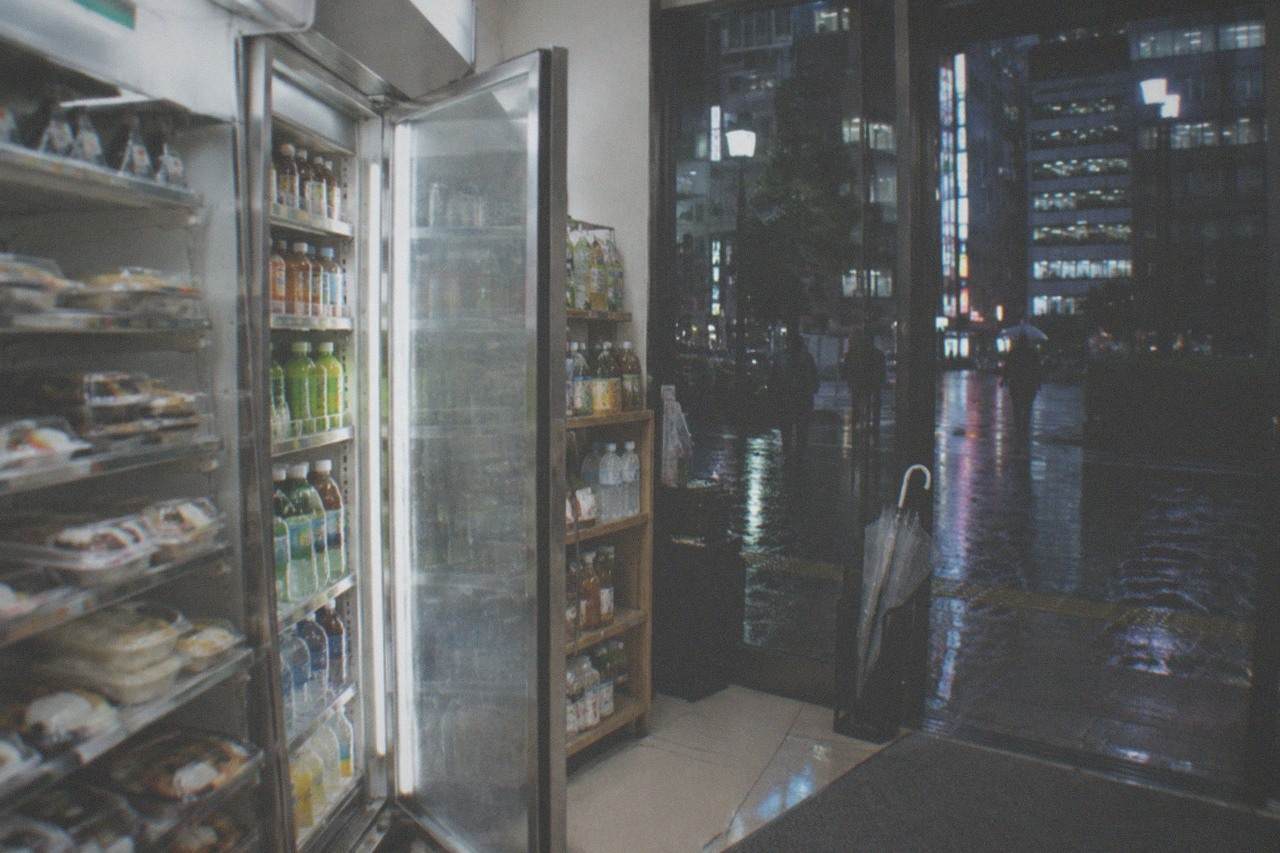 A brightly lit Japanese convenience store shelf at night with boxed meals and drinks on display
