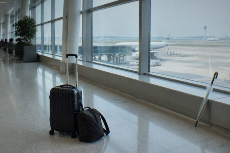 A wheeled suitcase and a smaller shoulder bag set down on the ground at a bright airport terminal walkway serving Tokyo, standing for the storage options travellers weigh before and after a flight.