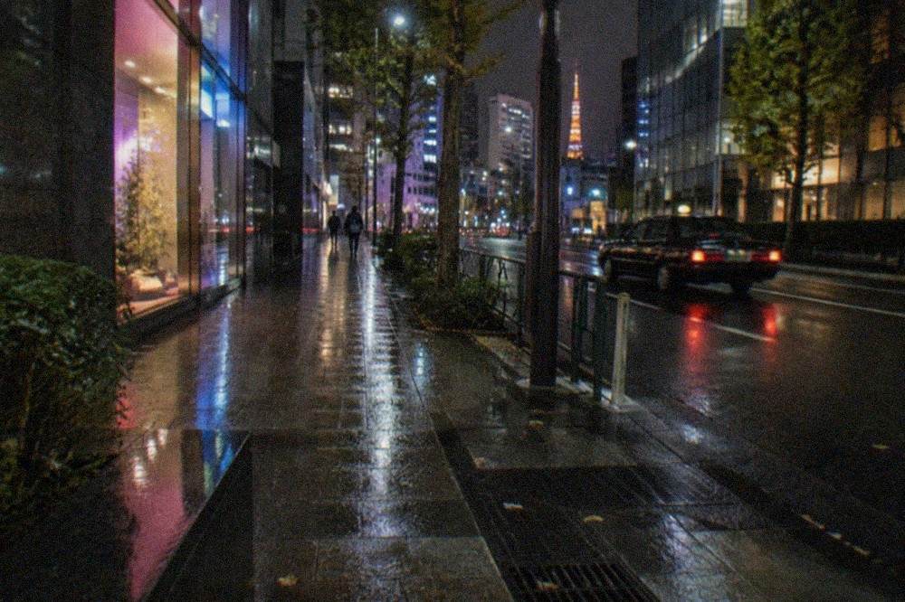 A dimly lit Tokyo street at night with neon shop signs and an empty sidewalk.