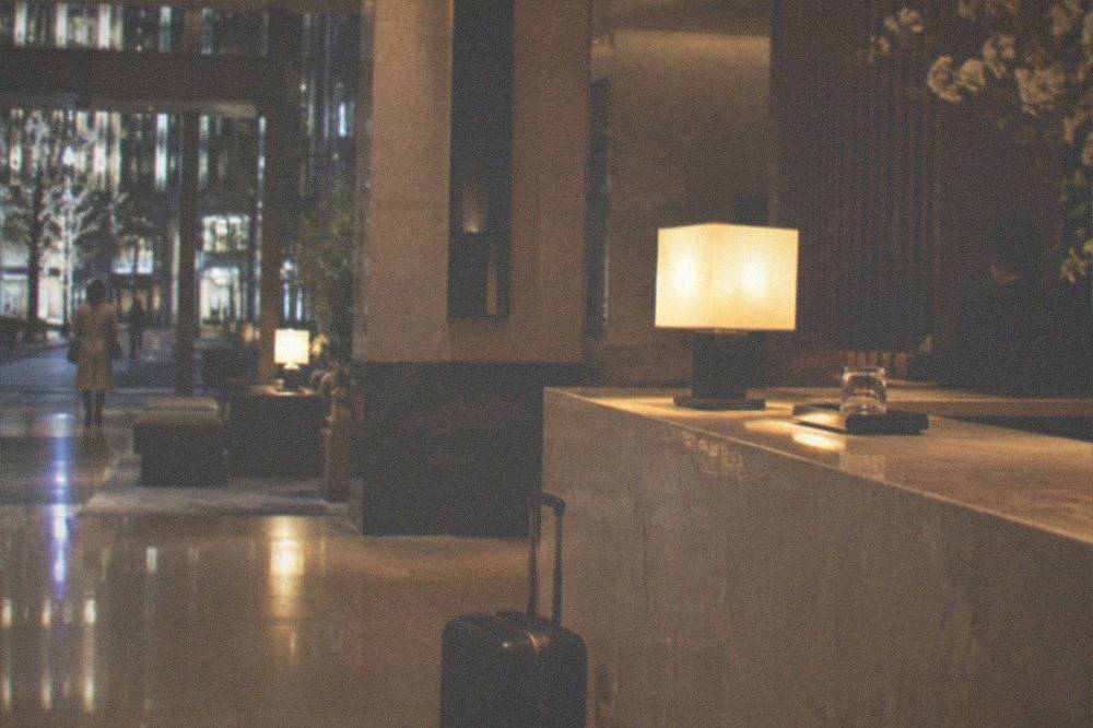A hotel front desk at night with a suitcase parked beside the counter under warm lighting.