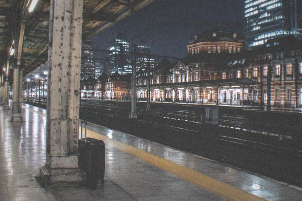 An empty Tokyo station platform late at night with a single suitcase waiting by a pillar.