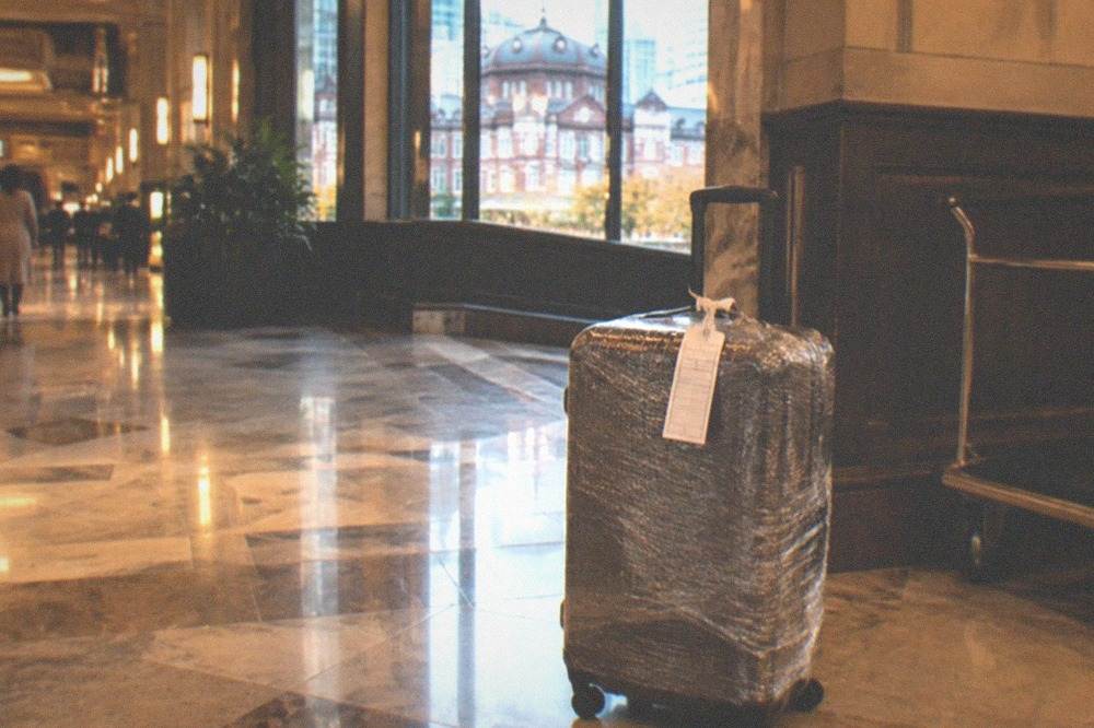 A wrapped suitcase with a courier waybill attached standing in a hotel lobby