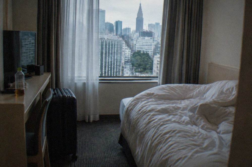 A narrow Tokyo hotel room with a single bed and a suitcase parked beside a small desk.