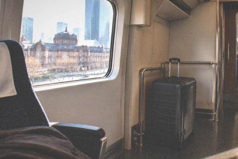 A large suitcase parked in the oversized luggage space beside Shinkansen seats