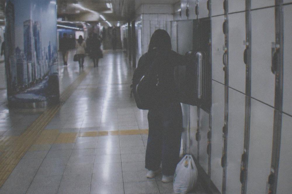 A traveller collecting a suitcase from a bank of coin lockers at night in a Tokyo station