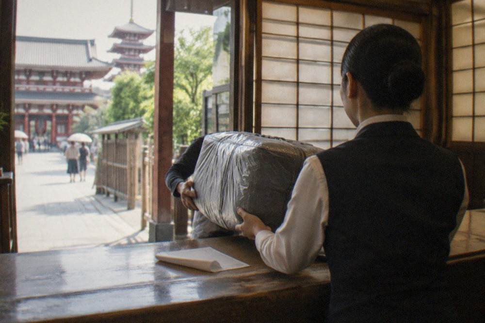 A hotel front desk clerk accepting a labelled suitcase for courier pickup