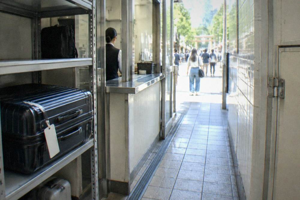 A tagged suitcase waiting inside a staffed bag storage point in a Tokyo district