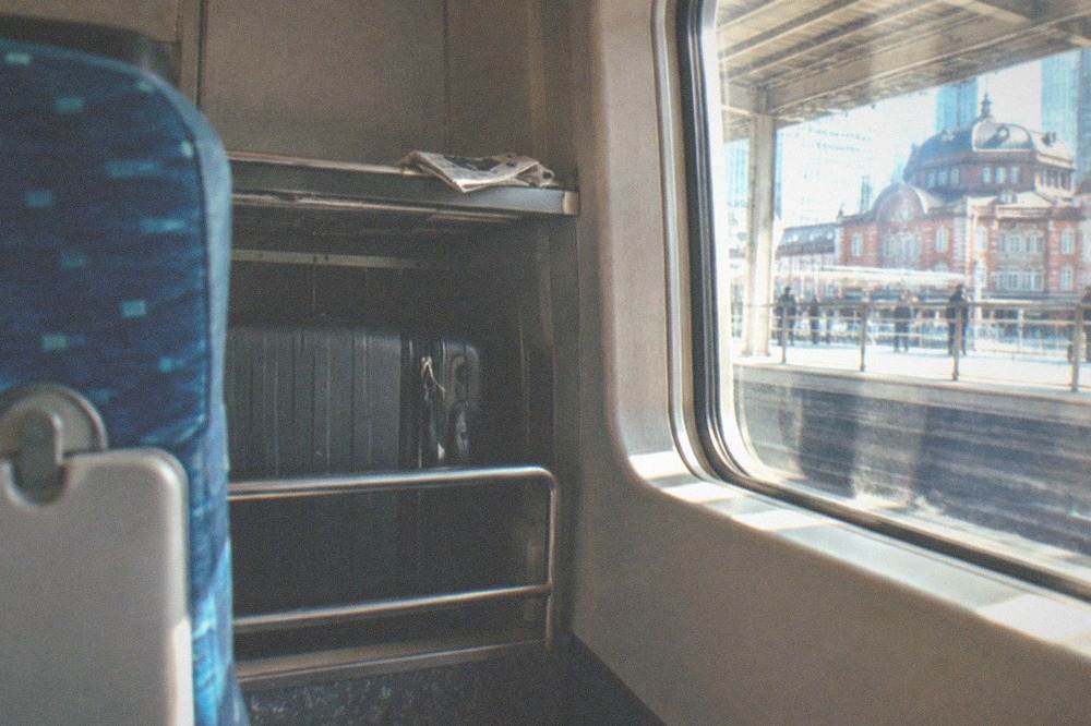 A wide suitcase parked in the dedicated luggage space behind a bullet train seat