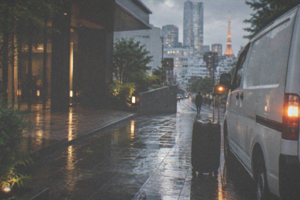 A suitcase standing beside a courier van at a Tokyo hotel entrance