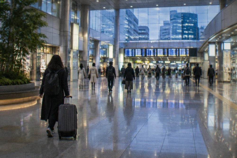 A traveler wheeling a large suitcase across a station concourse toward departure signs
