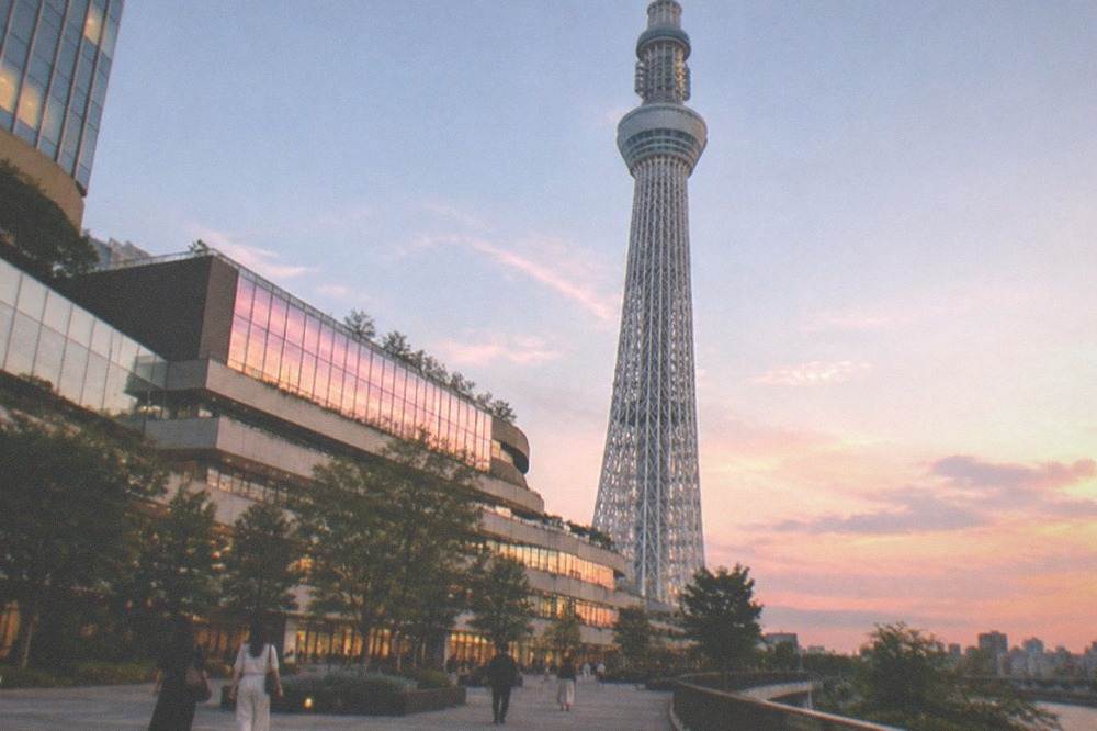 A tall broadcast tower rising above a shopping complex under a clear sky