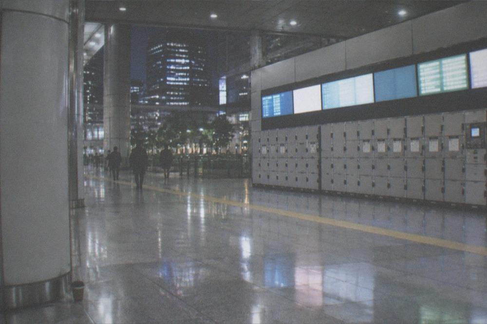 A wide station concourse at night with departure boards and a locked row of luggage lockers