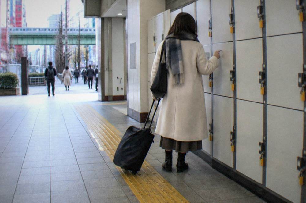 A row of coin lockers inside a Tokyo station with a woman selecting a door