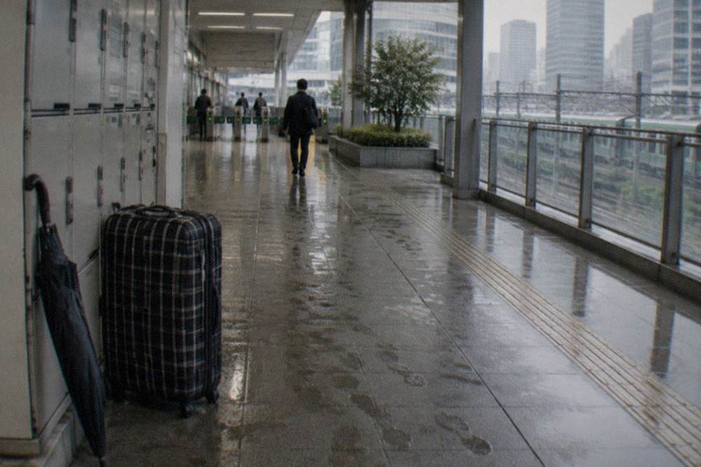 A wide checked suitcase parked next to a row of small coin lockers in a Tokyo station