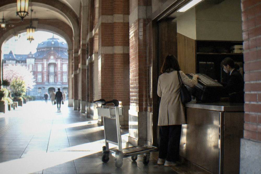 An oversized suitcase being handed over at a staffed baggage room counter in a Tokyo station