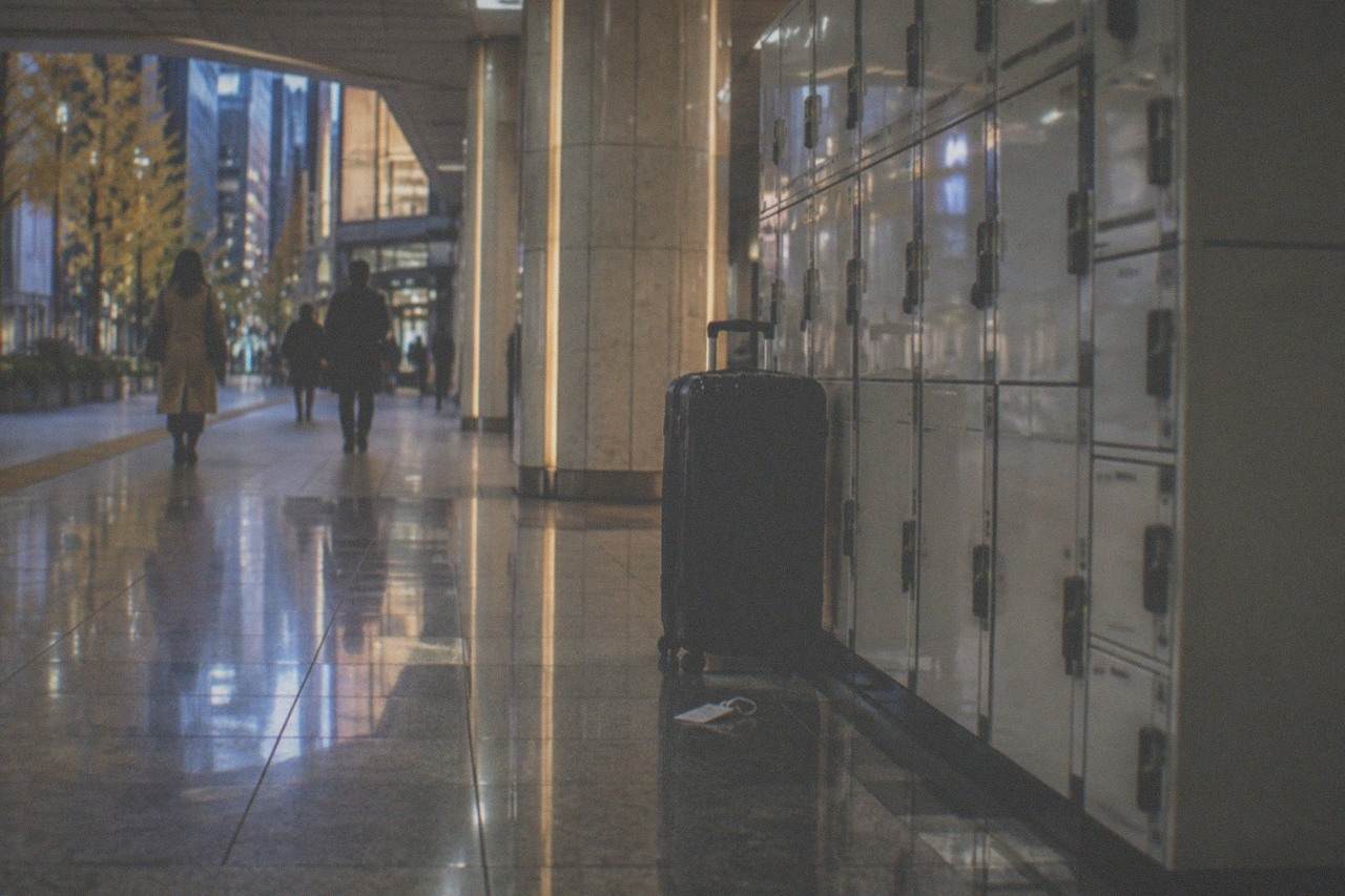 A large hard-shell suitcase standing beside a bank of coin lockers in a Tokyo station corridor