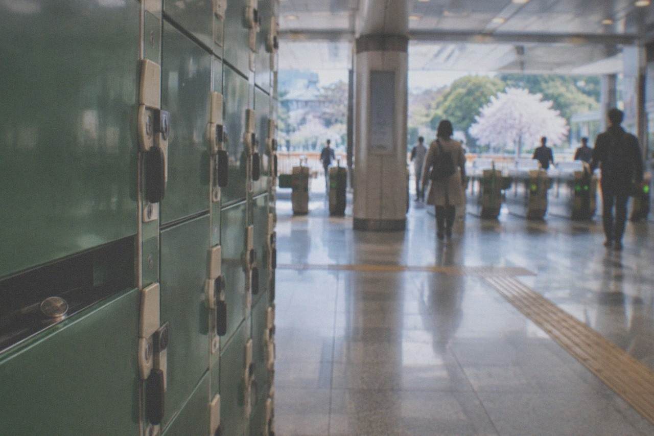 A bank of green coin lockers in a bright station corridor with a fare gate in the background