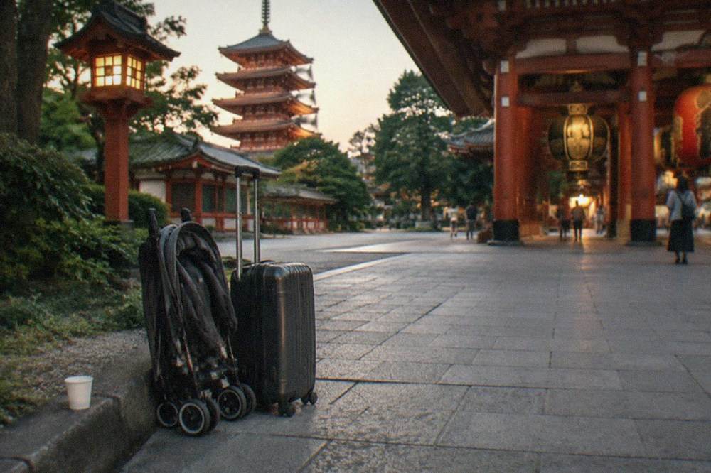 A folded stroller and a small suitcase parked on a wide pedestrian shopping street near a temple gate