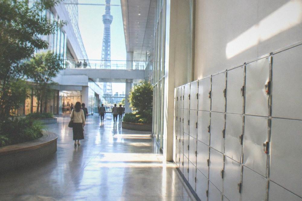 A bright shopping complex corridor with a row of coin lockers along one wall