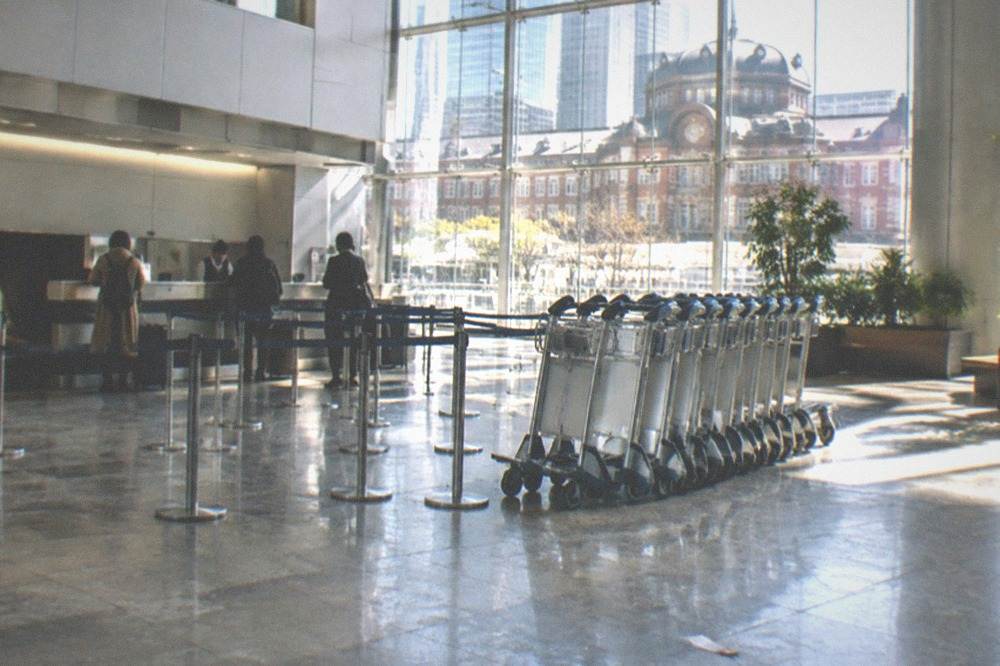 Airport terminal hall with an attended baggage counter and queues of trolleys, no people.