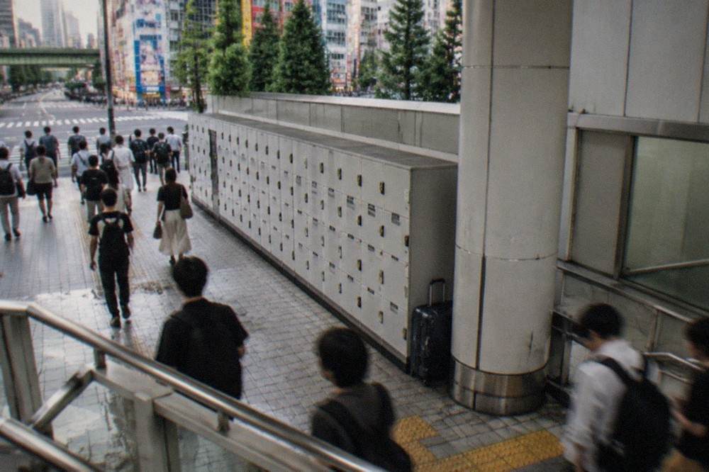 A crowded station concourse in Tokyo with a long bank of coin lockers along the wall